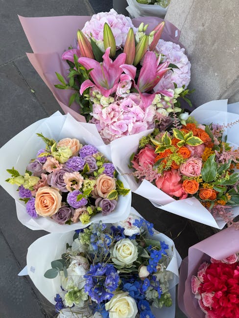A selection of five beautifully arranged floral bouquets placed on a grey outdoor surface, featuring a variety of fresh flowers. The largest bouquet showcases pink lilies and pink hydrangeas, wrapped 